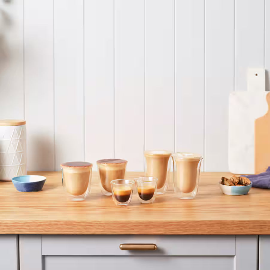 Row of glass cups with coffee on a wooden counter against a white paneled wall.